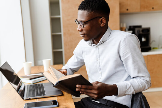 Afro american focused man reading book while working with laptop