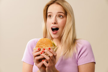 Surprised beautiful blonde girl posing with hamburger