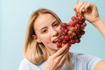 Pleased charming blonde girl eating grape on camera