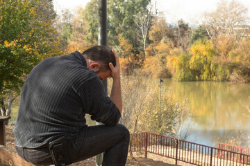 Hombre sentado en el borde de un banco, con expresión pensativa, frente a un río en invierno, depresivo