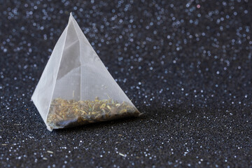 White transparent tea bag pyramid with green tea on a dark sparkling background. A drink for...