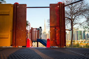 Little boy playing in the playground with Burj Khalifa, tallest building in the world in the background. Shot made from safa park. Outdoors