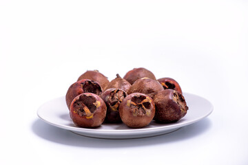 Fresh ripe organic common medlar fruit on a plate on white background. Healthy food Mespilus germanica