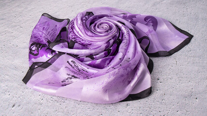 Iridescent light purple silk scarf folded in the shape of a rose on the gray plastered surface. Natural smooth soft fabric. 