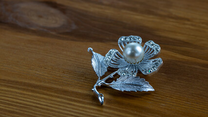 Silvery old brooch with iridescent real white pearl and sparkling crystals  on the natural dark brown wooden background. Isolated object, close up.