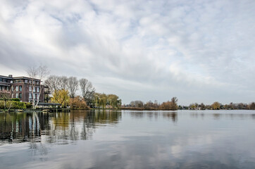 Fototapeta na wymiar Rotterdam, The Netherlands, December 13, 2020: one of the Bergsche Plassen lakes surrounded by suburban neighbourhoods under a sky with friendly clouds