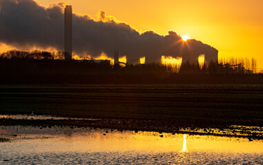 Sunrise at Drax. A Winter's morning with the sun rising behind a water vapour trail emitting from the cooling towers of a power station at Drax in North Yorkshire,  UK.  Horizontal.  Space for copy.