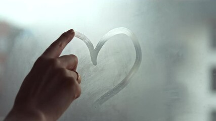 A hand draws a heart shape on the window with her finger. Fell in love. Shares love with the whole world and charity concept. Selective focus. - Powered by Adobe