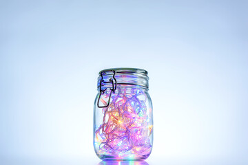 Glass jar with multi-colored glowing garland inside, blue background