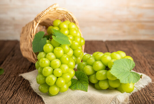 Green grape in Bamboo basket on wooden table in garden, Shine Muscat Grape with leaves in wooden background.