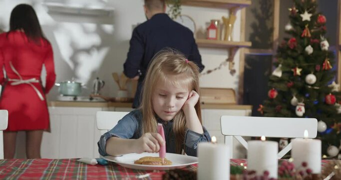 little girl intently paints gingerbread while her parents prepare dinner