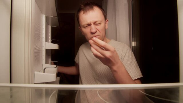 Man opens the refrigerator at night on the shelf is one cupcake, a disgruntled man
