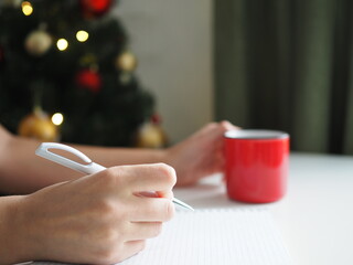 Women's hands write in a notebook on the background of Christmas lights. Goals 2021. Wish list. Shopping List
