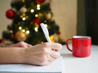 Women's hands write in a notebook on the background of Christmas lights. Goals 2021. Wish list. Shopping List