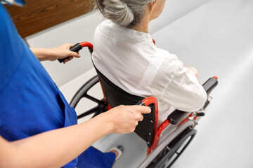 medicine, health and care concept - nurse taking senior woman patient in wheelchair at hospital corridor or nursing home