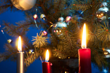 A candle flame on a background of decorated spruce branches of a Christmas tree