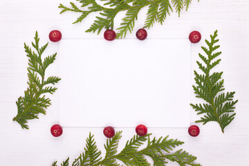 A flat composition with a Christmas decor, with live fir branches and an empty card lay on a white wooden table. Space for text
