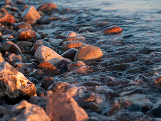 Rocks and pebbles on the beach being watered as the waves wash in on the beach at sunset