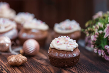 Chocolate muffin garnished with butter cream, pink and white sprinkles on a wooden table for New Year or Christmas.
Delicious christmas cupcake