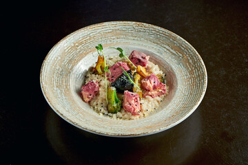 Italian risotto with baked salmon and broccoli in a plate on a black background