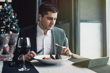 A young and attractive man uses his phone while eating veal tenderloin in ashes with grilled vegetables in an indoor restaurant