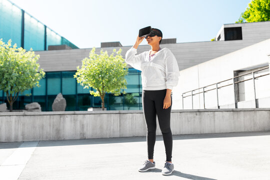 fitness, sport and technology concept - happy smiling young african american woman with virtual reality headset or vr glasses outdoors
