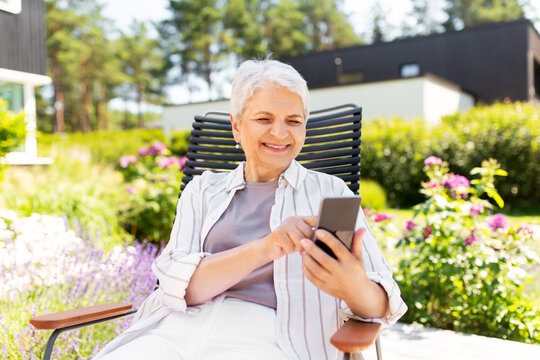 technology, old age and people concept - happy smiling senior woman with smartphone resting at summer garden