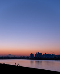 Sunset at Kyuedo River with silhouette of Mount Fuji and Maihama Great Bridge in the background and a person fishing by the river in the foreground.