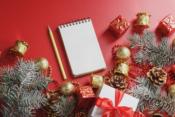 Notepad and pencil for writing wishes and gifts for the New Year and Christmas around the Christmas tree decorations on a red background.