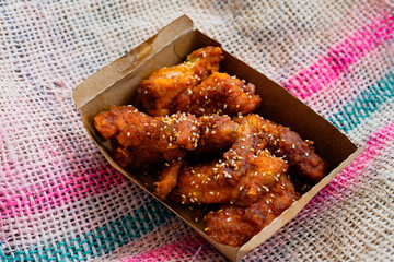 Deep fried chicken wings and drummets coated with hot and spicy Korean sauce in a take away container.