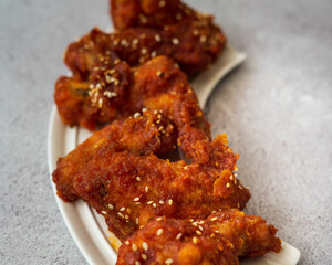 Deep fried chicken wings and drummets coated with hot and spicy Korean sauce on a white plate.