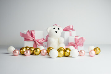 Festive background. White gifts with a pink ribbon and gold christmas balls on white background. Set of Christmas gifts on a white background. A white teddy bear is sitting among the gift.