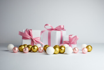 Festive background. White gifts with a pink ribbon and gold christmas balls on white background. Set of Christmas gifts on a white background. A white teddy bear is sitting among the gift.