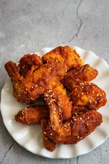 Deep fried chicken wings and drummets coated with hot and spicy Korean sauce on a white plate and green cloth.