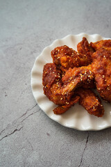 Deep fried chicken wings and drummets coated with hot and spicy Korean sauce on a white plate and green cloth.