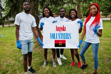 Group of happy african volunteers hold blank with Angola flag in park. Africa countries volunteering, charity, people and ecology concept.