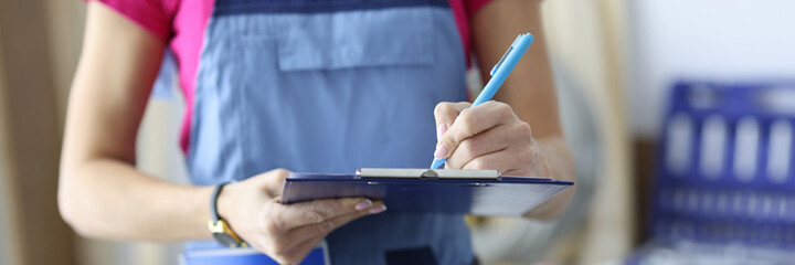 Woman builder in uniform writing with pen in document in workshop closeup. Provision of repair services concept