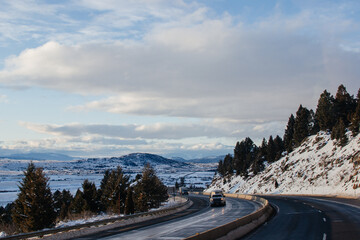 Highway in beautiful place in winer on the summer day. Landscape with asphalt road, trees, snow-covered mountain in winter. Montana, USA, 12-2-2019