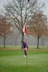 Middle-aged fit woman golfer putting for the hole on the green viewed from the flag concentrating...