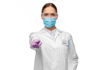 science, health and medicine concept - young female scientist wearing goggles and face protective medical mask for protection from virus pointing to camera
