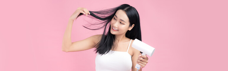 Beautiful Smiling Asian Girl With Black Long Straight Hair Using Hairdryer. Isolated on pink...