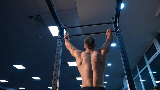 Handsome man gumped on horisontal bar. Male sportsman trains in gym. Slow motion.