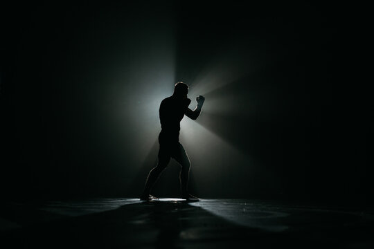 Fighter striking a blow. Professional sport. Fighting. Strength. Fighter in a moody light and grain mood.
boxer training with punching bag in dark sports hall
