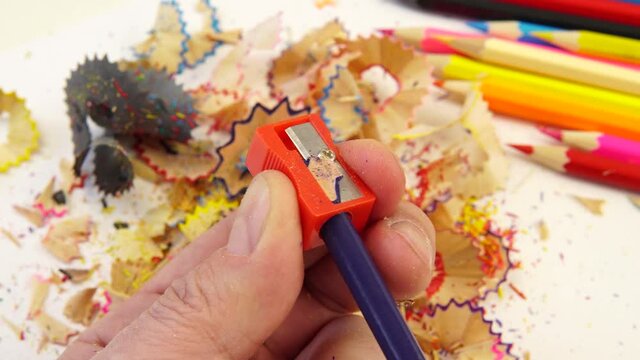 Dad sharpens pencils for a child. A man holds a sharpener in his hands and sharpens colored pencils. Person's viewing point, first perspective. Homework concept.