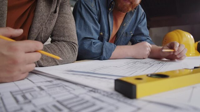 Close up shot of two male architects discussing floor paper plan on table during workday at construction site