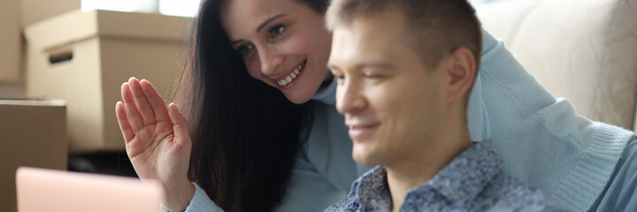 Man and woman communicating via laptop video link and waving hand at home. Remote meeting during pandemic concept