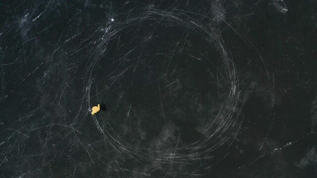 Aerial top view of a man ice skating outdoors on frozen water reservoir. Male ice skating on frozen lake, drawing circles on ice