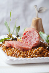 Italian large pork sausage cotechino served  with lentils on white plate.