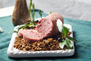 Italian large pork sausage cotechino served  with lentils on white plate.