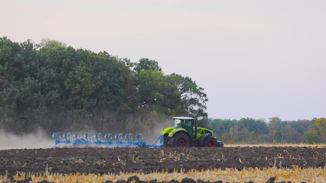 Green tractor plows the field. Tractor in the field. A modern tractor plows the field.